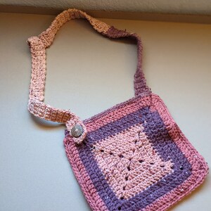 May include: A crocheted pink and purple shoulder bag with a wooden button closure.