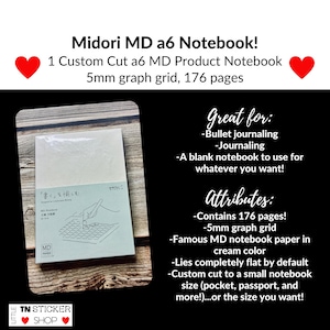 May include: A Midori MD A6 notebook with cream-colored paper and a 5mm graph grid. The cover features a line drawing of a hand writing on a grid, the text "MD Notebook," and Japanese characters. The notebook contains 176 pages in total.