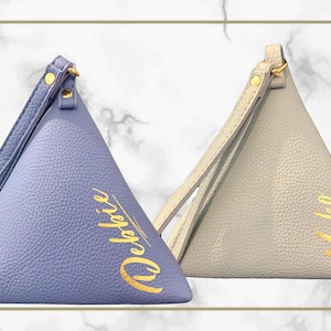 May include: Two triangular pouches, one periwinkle and one light gray, with gold lettering and wrist straps. The periwinkle pouch has the name "Debbie" in gold script, and the light gray pouch has the name "Yuko". Both have gold hardware.