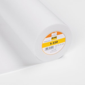 Könnte beinhalten: Eine weiße Rolle Vlieseline S 320 Einlage. Das Etikett ist gelb mit schwarzem Text und einem Barcode. Das Etikett lautet "100% PES 90 cm x 25 m".