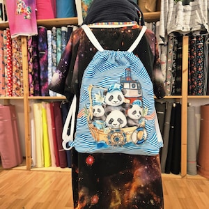 Könnte beinhalten: Blauer Rucksack mit Kordelzug und nautischem Panda-Design. Die Pandas tragen Matrosenmützen auf einem Boot, umgeben von Wellen, einem Schiff und einer Rettungsboje. Der Rucksack hat weiße Träger.