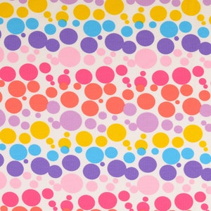 Könnte beinhalten: Ein weißer Stoff mit einem sich wiederholenden Muster aus bunten Kreisen. Die Kreise sind in diagonalen Reihen angeordnet und in den Farben Gelb, Blau, Rosa und Lila gehalten.