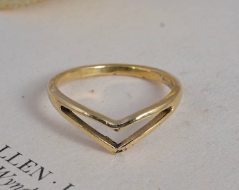 May include: A gold-coloured ring featuring a double V-shaped design. The ring is made of metal and rests on a white surface. The ring's design is simple and elegant, with a polished finish.