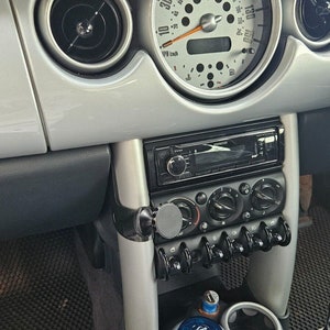 Peut inclure: L'intérieur d'une Mini Cooper argentée avec un tableau de bord noir, une radio noire et un pommeau de levier de vitesses noir. La voiture a un tapis de sol noir et gris.