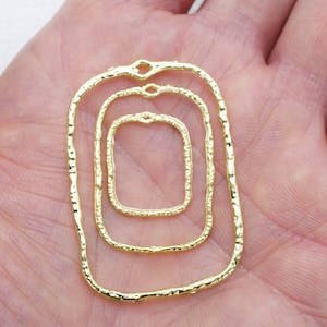 Pode incluir: Três molduras retangulares de metal dourado de diferentes tamanhos, com uma superfície texturizada, estão aninhadas umas nas outras. As molduras são abertas na parte superior e inferior, e têm um pequeno laço na parte superior.