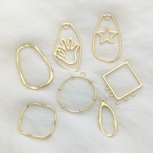 May include: A set of seven gold-toned metal pendant blanks, each with a different shape, including a circle, square, oval, and hand. The blanks are perfect for crafting jewelry or other DIY projects.