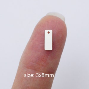 Puede incluir: Una peque&ntilde;a etiqueta de metal blanco con un agujero en la parte superior. La etiqueta es rectangular y mide 3 por 8 mil&iacute;metros.