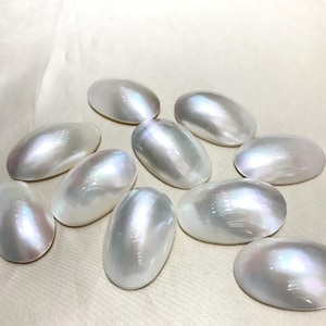 Peut inclure: Dix cabochons ovales en nacre blanche irisée. Les cabochons sont lisses et polis.