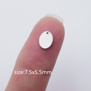 Puede incluir: Un charm ovalado de plata con un agujero en la parte superior. El charm mide 7,5 mm por 5,5 mm.