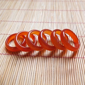 Puede incluir: Cinco anillos de cornalina naranja apilados en una estera de bambú. Los anillos son lisos y pulidos.