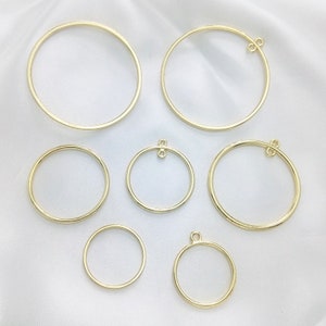 Pode incluir: Conjunto de sete argolas de metal dourado de tamanhos diferentes. As argolas são lisas e têm um acabamento polido. Algumas das argolas têm um pequeno laço na parte superior.