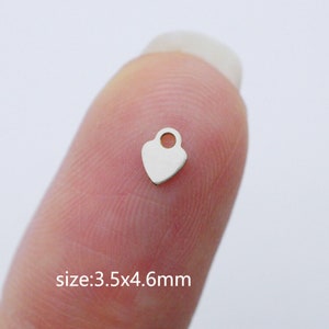 Puede incluir: Un peque&ntilde;o charm de coraz&oacute;n plateado con un bucle en la parte superior. El charm mide 3,5 x 4,6 mm.
