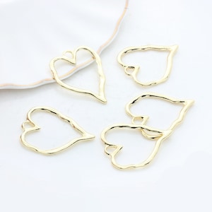May include: Five gold-colored metal heart-shaped pendant frames. The frames have a textured, hammered finish.