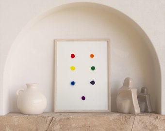 Könnte beinhalten: Ein gerahmter Druck mit weißem Hintergrund und bunten Punkten in Regenbogenfarben. Der Druck wird auf einem Holzregal mit zwei Keramikskulpturen ausgestellt.