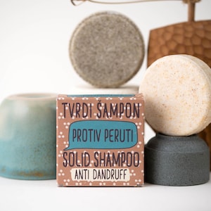 May include: A collection of solid shampoo bars and a box of solid shampoo. The box is brown with white polka dots and text that reads "TVRDI SAMPON PROTIV PERUTI SOLID SHAMPOO ANTI DANDRUFF". The shampoo bars are round and in shades of grey and beige.