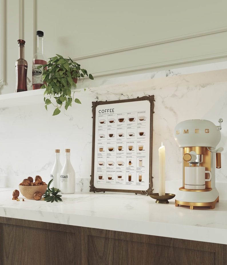 Op de afbeelding: Een witte en gouden Smeg espressomachine met een glazen kan en een witte kop op het aanrecht. Achter de machine hangt een ingelijst poster met de tekst "COFFEE THE ESSENTIALS" en een schema van verschillende koffiedrankjes. Er staan twee doorzichtige glazen flessen met witte etiketten en een kom met walnoten op het aanrecht.