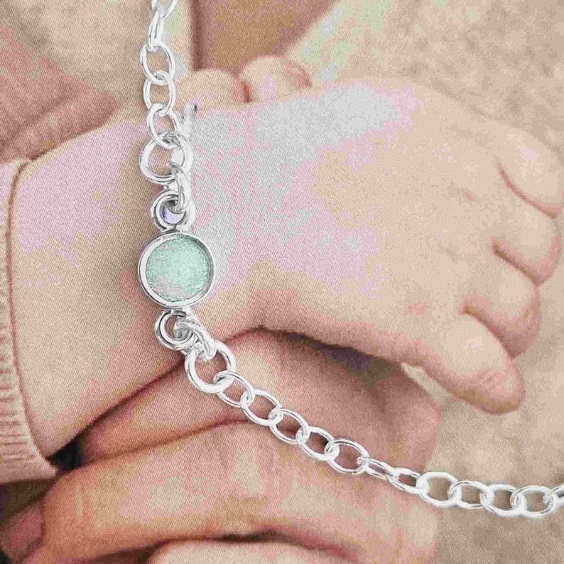 May include: A silver chain bracelet with a round, light blue charm. The charm has a sparkly, iridescent finish.