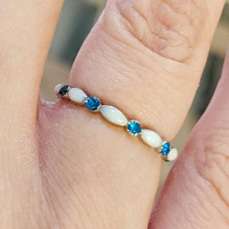 May include: A silver ring with white oval-shaped stones and blue gemstones.