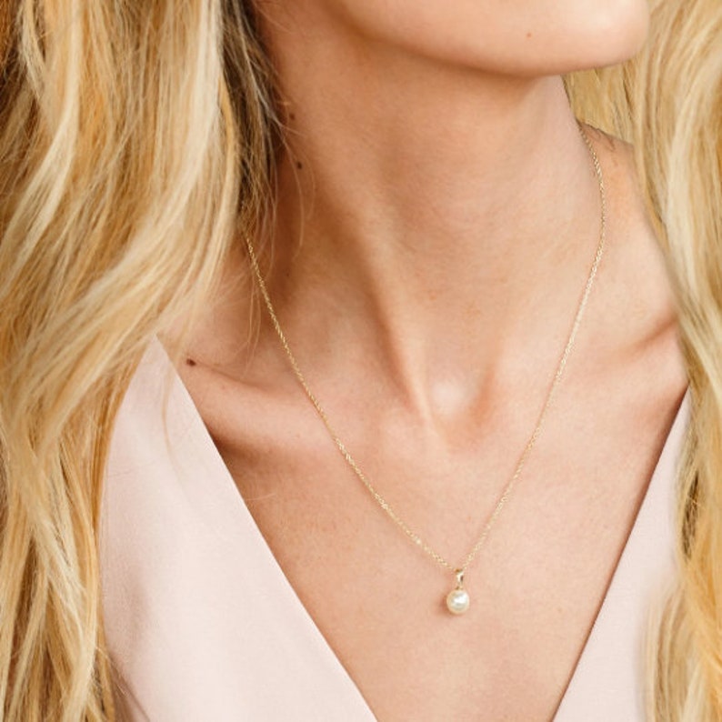 May include: A delicate gold chain necklace with a single, small, white pearl pendant.