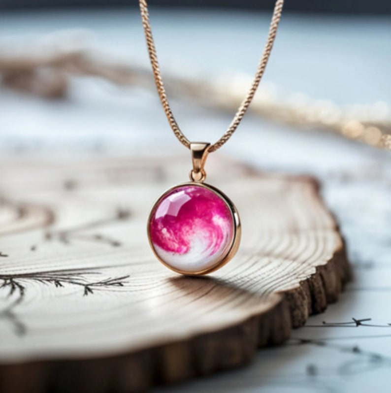 May include: A gold chain necklace with a round pendant featuring a pink and white swirl design.
