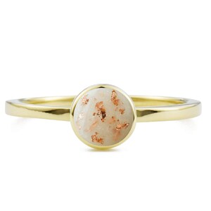 May include: A gold ring with a white stone set in the center. The stone is covered in small, gold flecks.