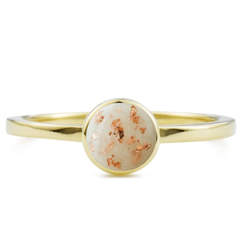 May include: A gold ring with a white stone set in the center. The stone is covered in small, gold flecks.