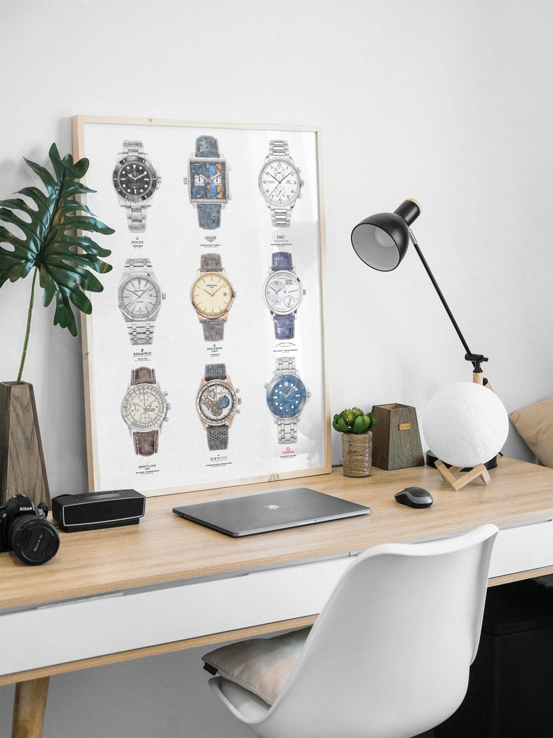 May include: A framed poster with illustrations of 12 different wristwatches. The poster is hanging on a white wall above a wooden desk with a laptop, a lamp, and a moon lamp.