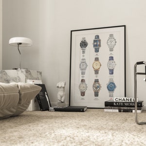 May include: A black framed poster with a white background featuring a collection of 12 different wristwatches. The watches are arranged in four rows of three. The poster is hanging on a white wall in a room with a white couch, a white lamp, and a white marble side table.