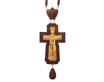 May include: An ornate wooden Orthodox cross pendant with a gold-coloured Jesus figure. The cross has detailed carvings and hangs from a brown cord. The pendant includes a crown-like top and a decorative teardrop-shaped bottom element.