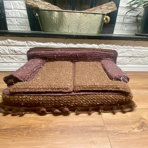 May include: A brown crocheted couch with a ruffled edge. The couch is made of a brown and dark brown yarn.