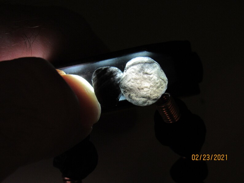 May include: A close-up of a bracelet featuring two light-colored, textured stones. The stones are illuminated, revealing their rough surfaces. The bracelet has black beads and a copper-colored coil.