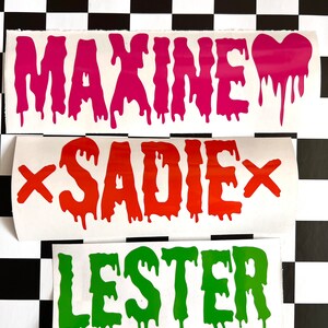 May include: Three white vinyl stickers with dripping letters spelling out the names "Maxine", "Sadie", and "Lester". The letters are pink, orange, and green, respectively.