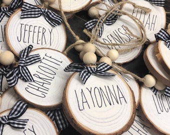 May include: A collection of round wooden ornaments with names written in black ink. Each ornament has a black and white checkered ribbon tied around it and a string of wooden beads.