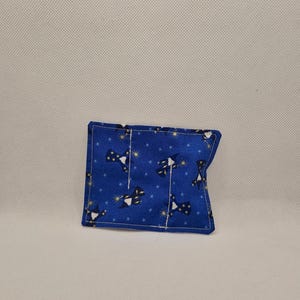 May include: A small, blue fabric pouch featuring a pattern of black and white figures and gold stars. The pouch is rectangular and appears to be handmade.