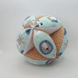 May include: A multi-coloured fabric ball with a variety of animal faces and star patterns. The ball is made of soft fabric and is designed for babies and toddlers.