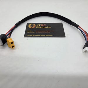 Puede incluir: Un cable negro con conectores en cada extremo, con cables rojos, blancos y azules. Un extremo tiene un conector amarillo y el otro un conector blanco. También hay una tarjeta de visita con el texto "JTRC Electronics".