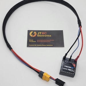 May include: A black cable with red, blue, and black wires, connected to a black and gray Protek LIHV 420 component. A yellow connector is visible. A business card with the JTRC Electronics logo and contact information is also present.