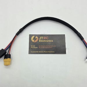 Puede incluir: Un cable negro con conectores en cada extremo, con cables rojos, azules y negros. También hay un conector amarillo. Una tarjeta de visita con el texto "JTRC Electronics" e información de contacto está en el centro.