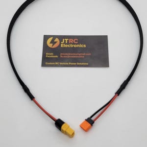Pode incluir: Um cabo preto com fios vermelhos e pretos e conectores amarelos e laranja. O cabo está conectado a um cartão de visita com o logotipo da JTRC Electronics e o texto "Custom RC Vehicle Power Solutions."