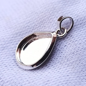 May include: Silver teardrop pendant with a smooth, rounded surface and a loop at the top for attaching a chain.