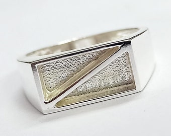 Op de afbeelding: Een zilveren ring met een geometrisch ontwerp. De ring heeft een getextureerd oppervlak en een rechthoekige vorm.