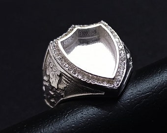 Op de afbeelding: Een zilveren ring met een schildvormige zetting, omringd door kleine heldere stenen. De ring is ontworpen om een cameo of ander decoratief element te bevatten.