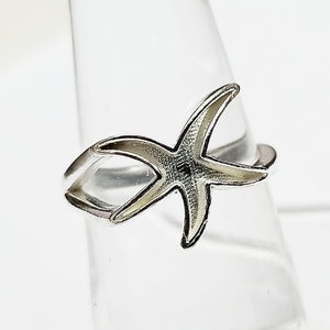 Pode incluir: Um anel de prata com um design de estrela do mar. A estrela do mar está aberta de um lado e o anel é ajustável.