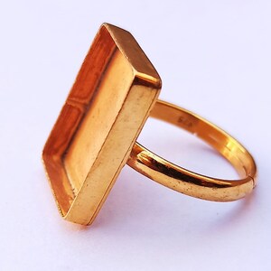 Puede incluir: Anillo dorado con engaste cuadrado. El engaste está vacío y listo para ser rellenado con resina o una piedra preciosa.