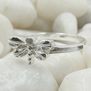 Könnte beinhalten: Ein silberner Ring mit einem Libellen-Design. Die Libelle ist detailliert und hat eine strukturierte Oberfläche.