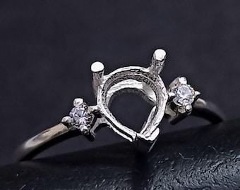 May include: A silver ring setting with a pear-shaped centre stone and two smaller round stones on the band.