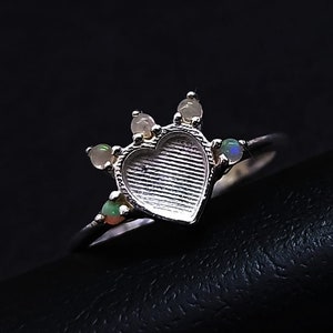 May include: A silver ring with a heart-shaped setting and five small opal stones. The ring is on a black surface.