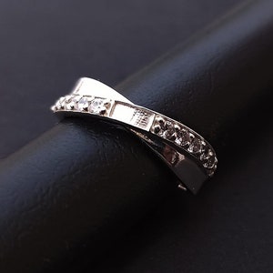 Op de afbeelding: Een zilveren ring met een kruislings ontwerp en kleine heldere stenen die in de band zijn gezet.