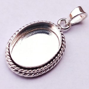 Puede incluir: Pendiente de plata con un borde de cuerda, diseñado para sujetar un camafeo u otro elemento decorativo. El pendiente tiene un aro para sujetarlo a una cadena.