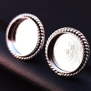 May include: Two silver-toned metal earring settings with a rope-like edge. The settings are round and have a smooth, reflective surface.